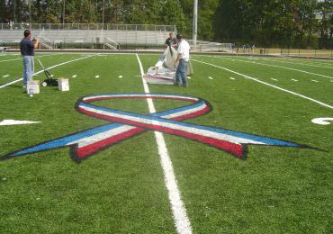 Ribbon stencil painted on synthetic field turf football field.