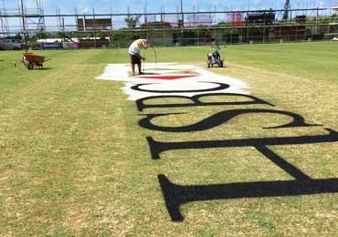 Corporate logo being painted on cricket pitch.