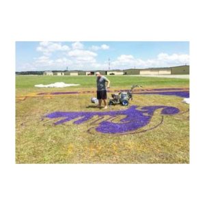 Workers Painting Purple Corporate Logo On A Grassy Field